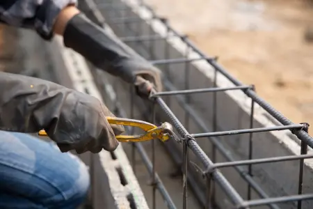 Bauarbeiter mit Handschuhen befestigt Stahlstangen auf einer Baustelle.