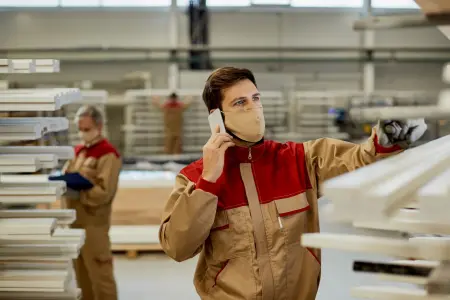 Ein Arbeiter mit Gesichtsmaske telefoniert, während er in einer Tischlerei arbeitet.