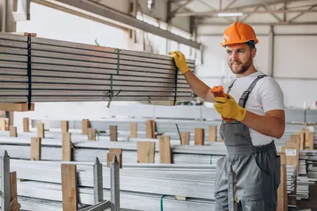 Ein Arbeiter in einer Lagerhalle trägt einen orangefarbenen Helm und überprüft Materialien.