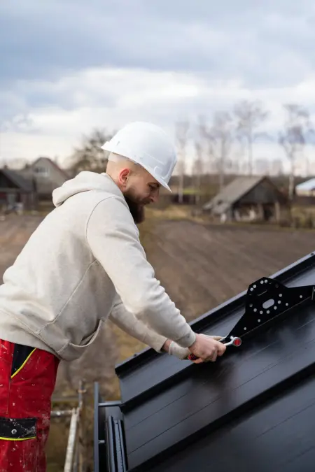 Ein lachelnder Mann mit Schutzhelm arbeitet an einem modernen Dach mit innovativen Materialien.